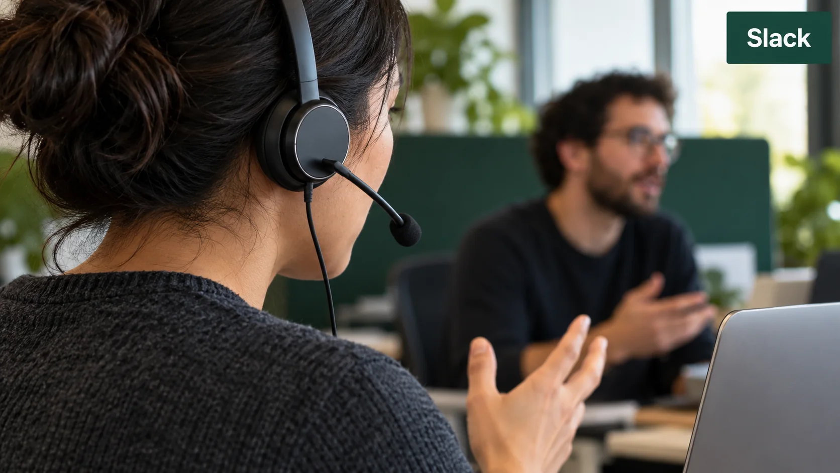 A close crop of a wired headset user speaking in a shared workspace, with a small Slack label.